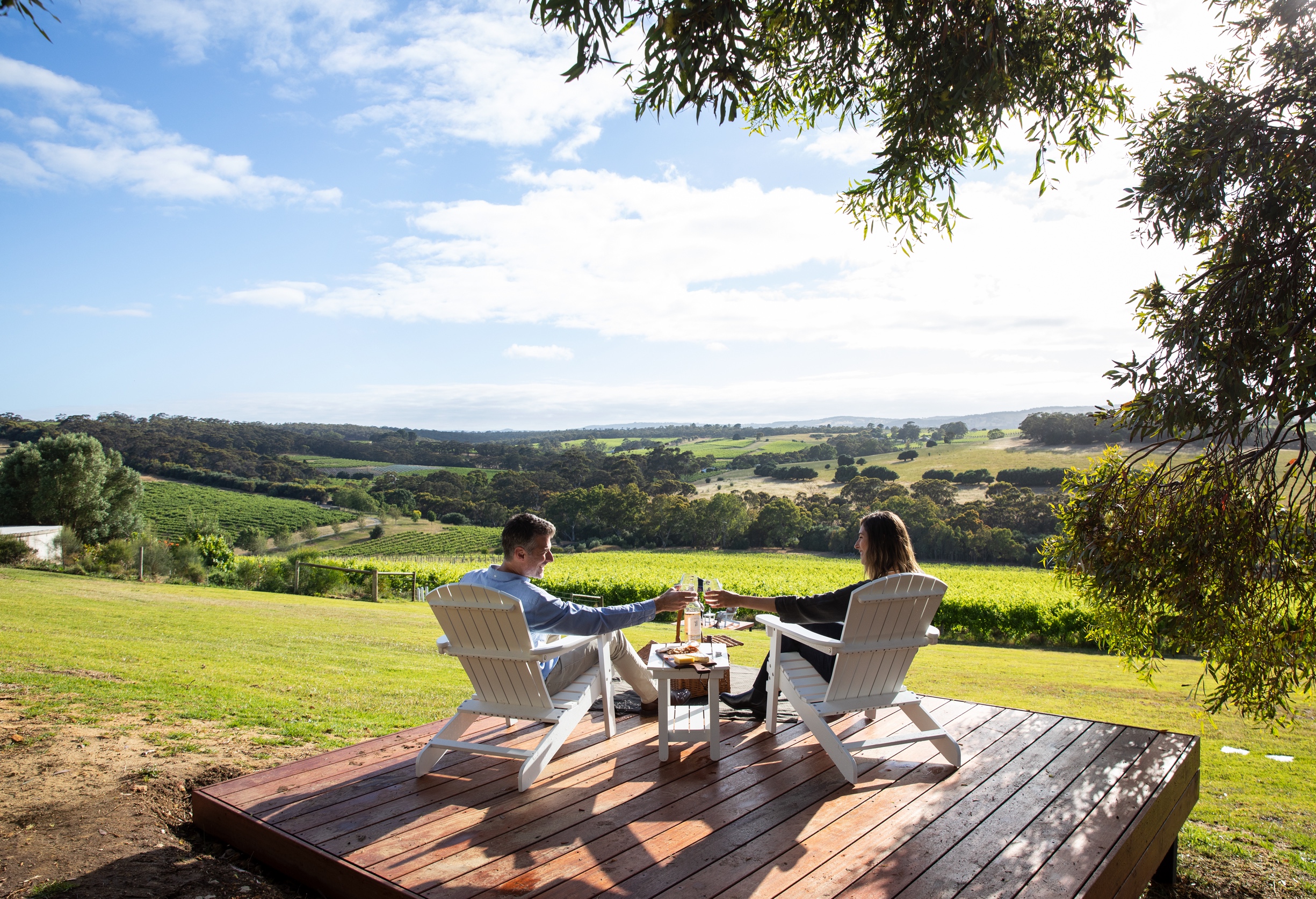 Man and woman sitting overlooking the winery grounds with wine and cheese. 